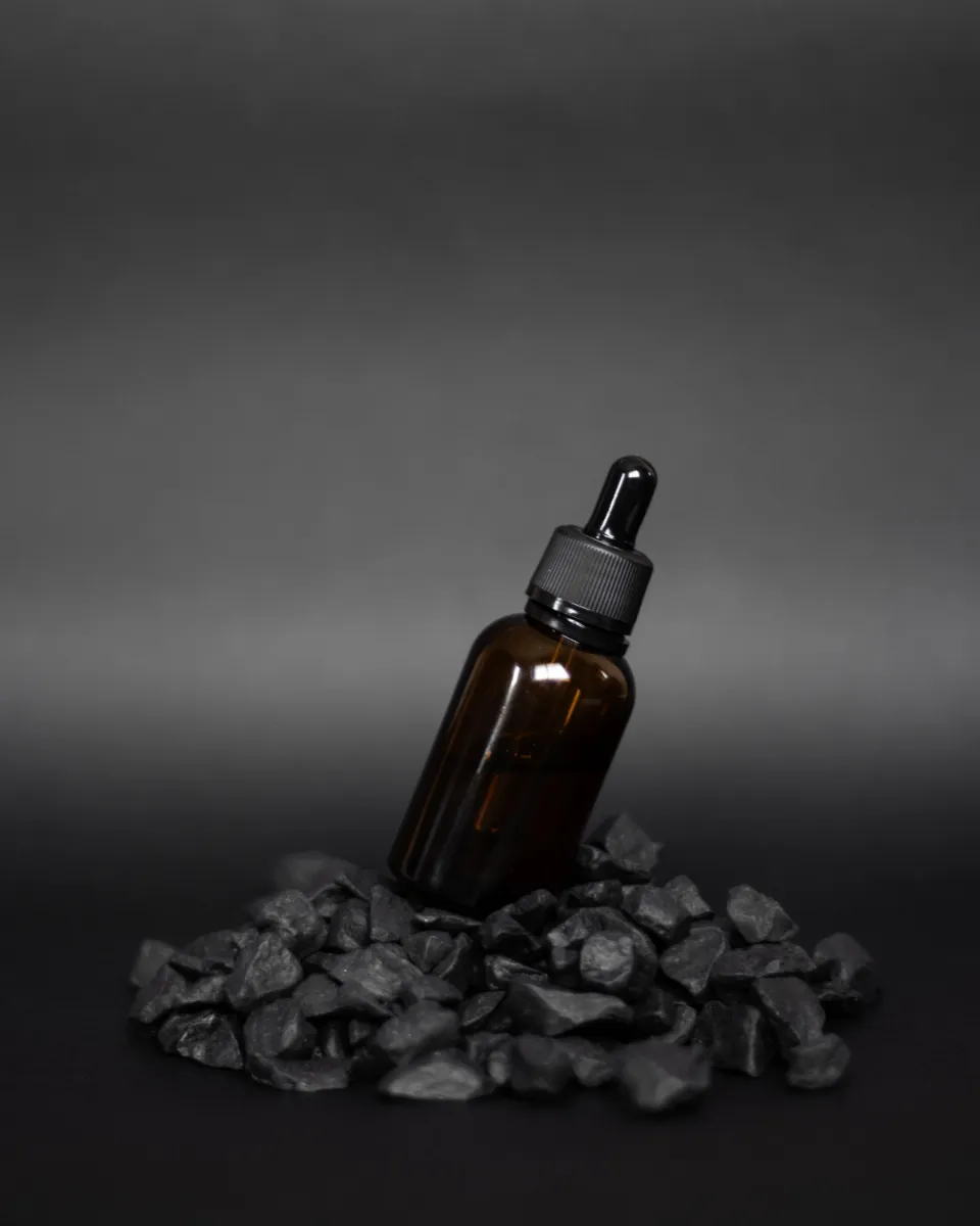 An amber glass dropper bottle resting on dark stones against a charcoal background.